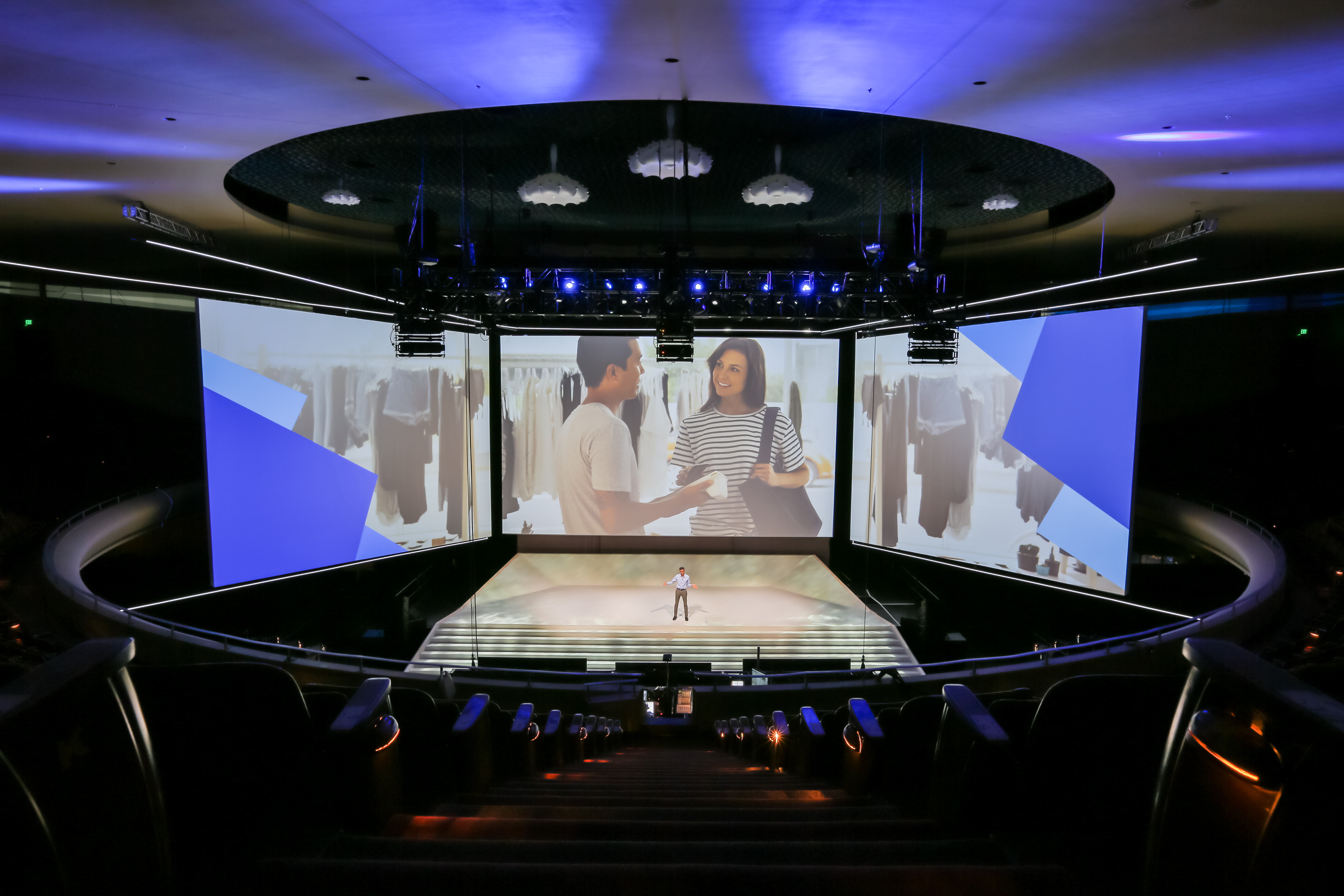 Man presents on stage at a corporate event at a Live Nation Specials Events venue surrounded by video monitors